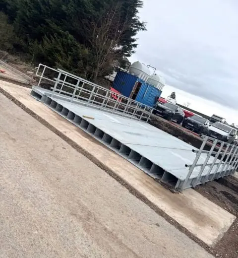 Installed steel bridge with handrails beside a workshop yard.